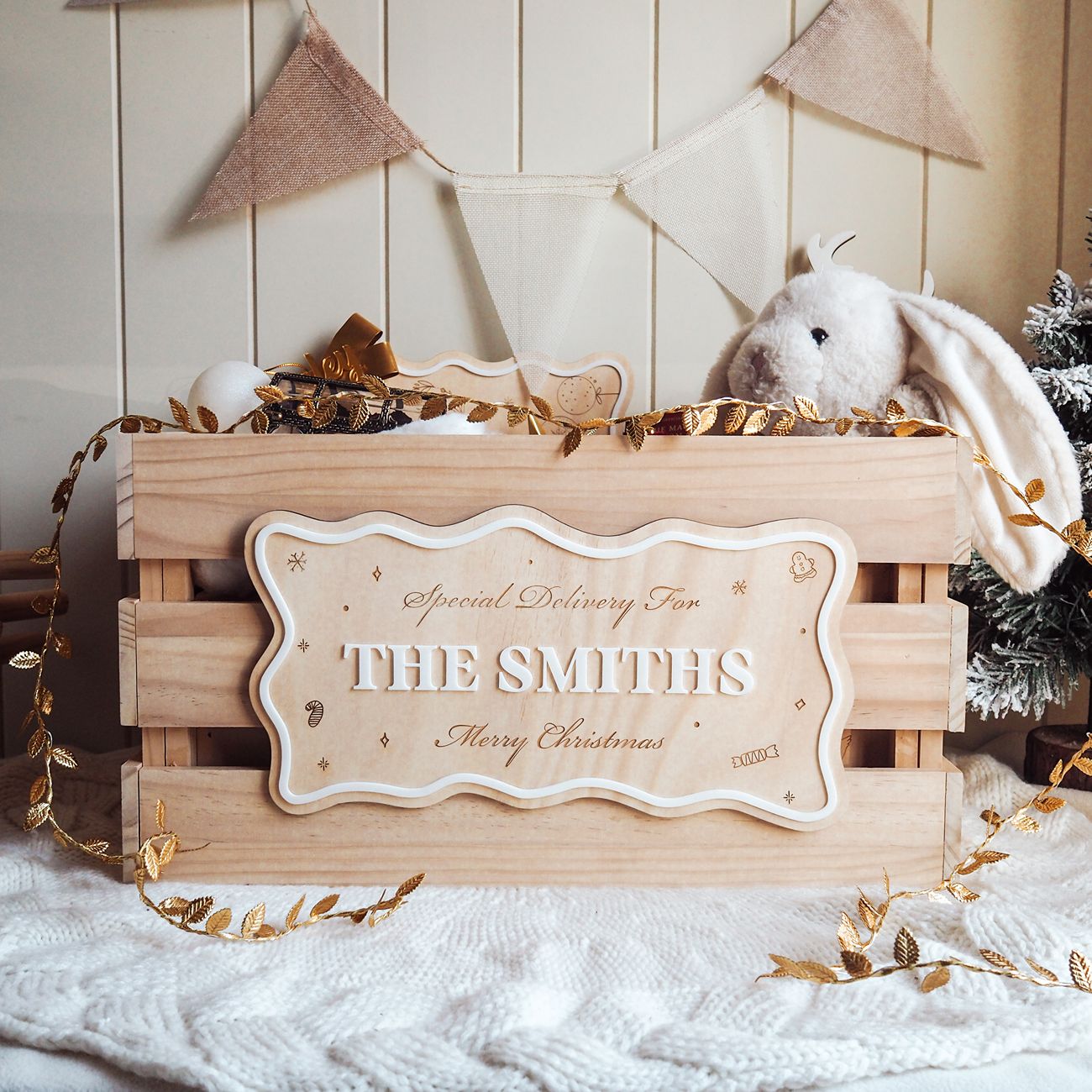 Wooden crate with 'The Smiths' sign, teddy bear, and Christmas decorations on a white surface.