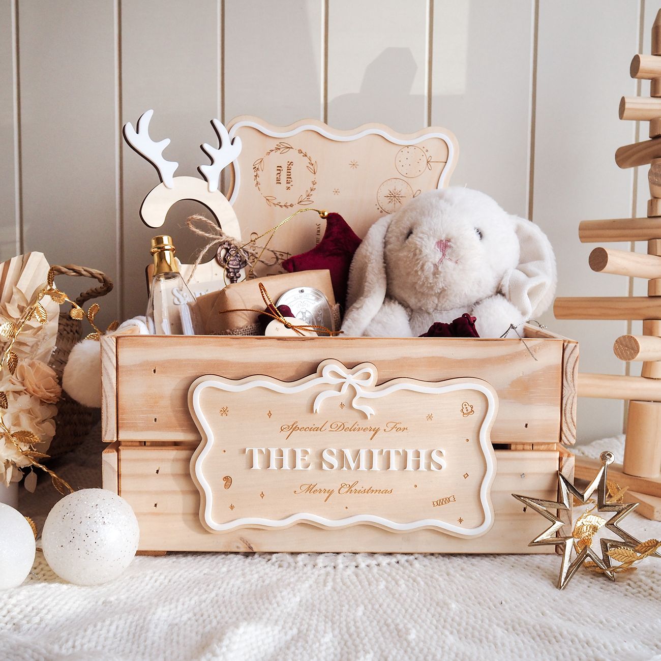 Wooden gift box with 'The Smiths' engraving, stuffed rabbit, and Christmas decor on a soft surface.