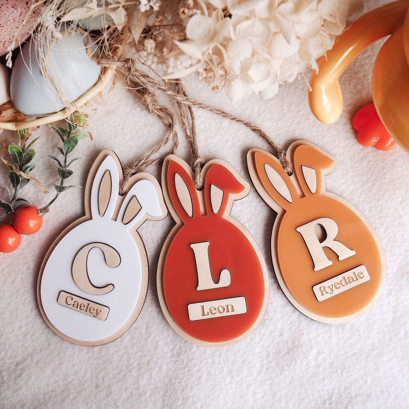 Three decorative bunny-shaped tags with names on a textured surface.