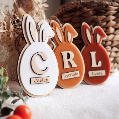 Three decorative bunny-shaped ornaments with letters and names on a soft surface.