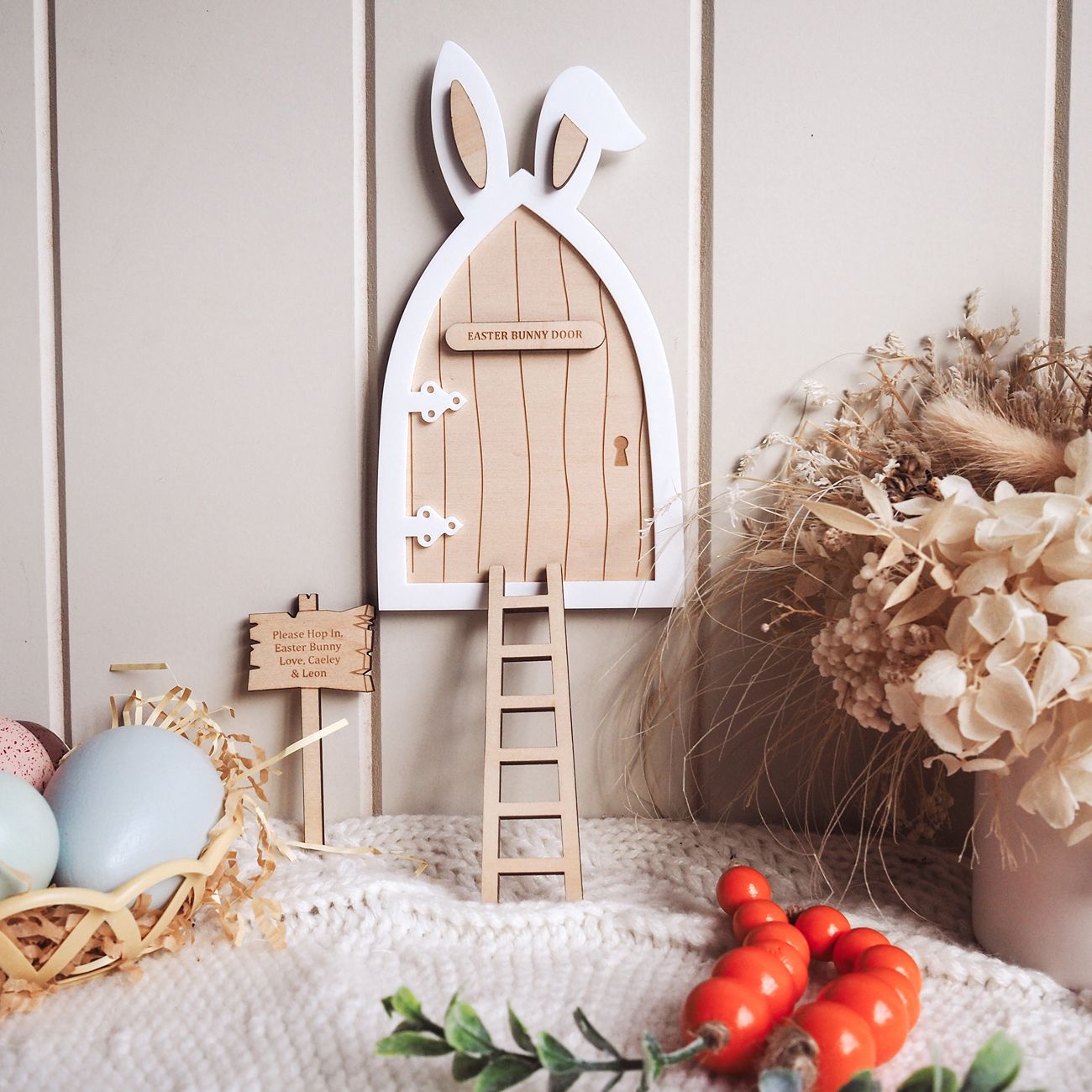 Wooden Easter door with rabbit ears, eggs, and flowers on a soft surface.