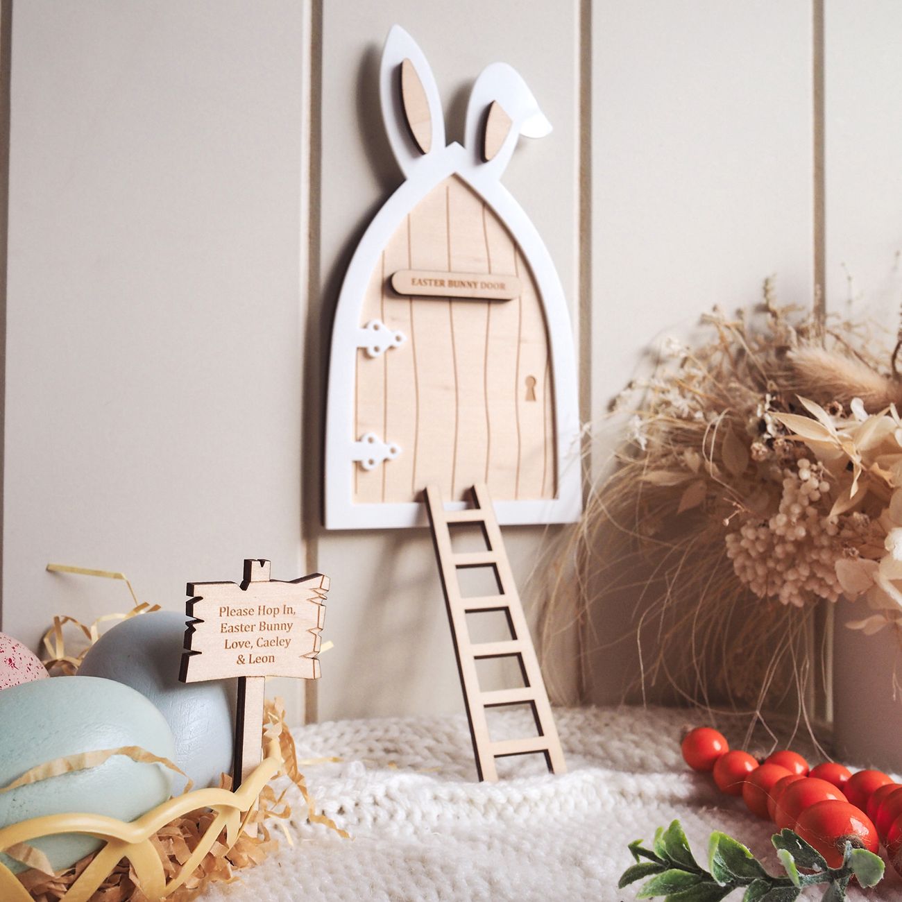 Wooden Easter bunny door with a ladder on a decorative surface with eggs and flowers.