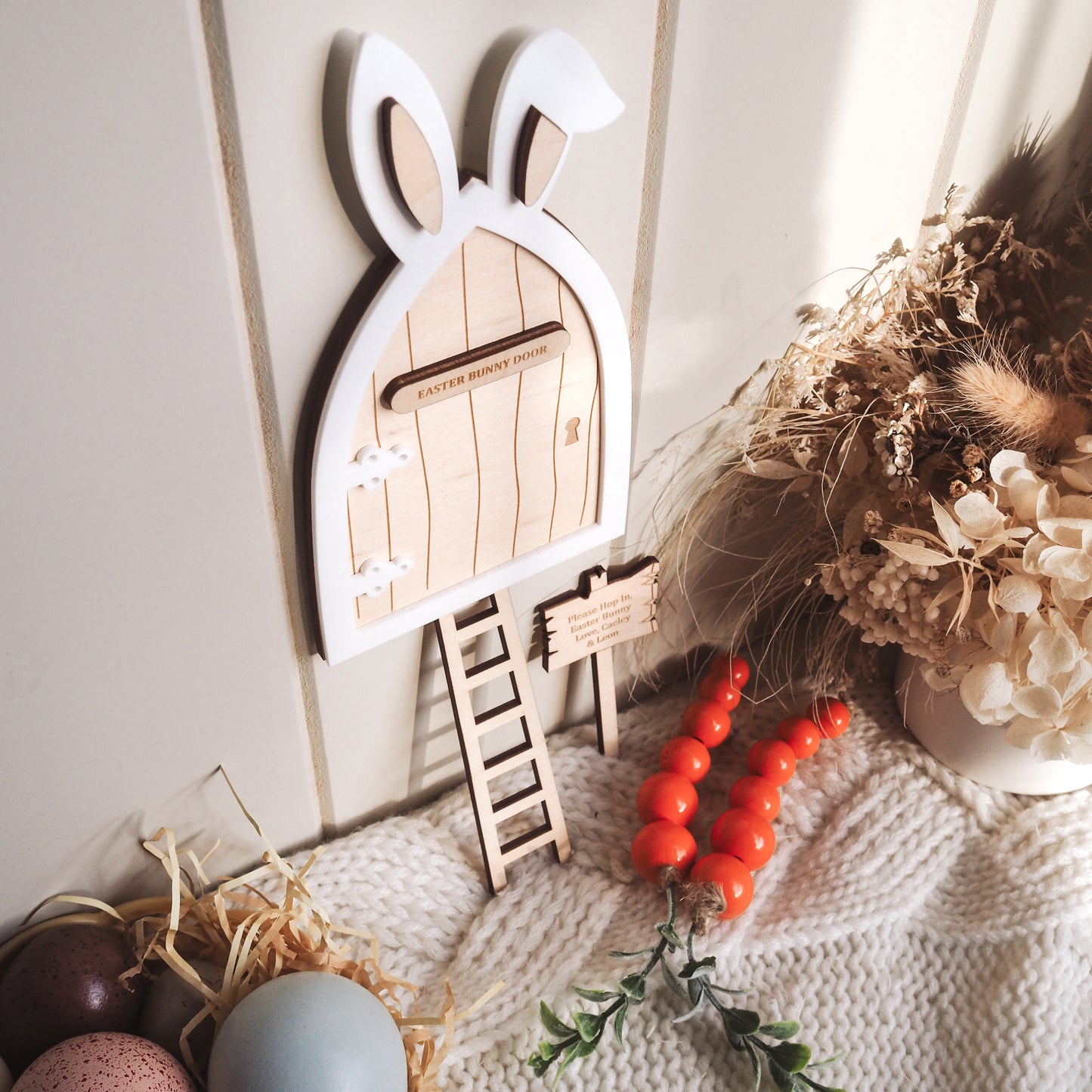 Wooden bunny door with a ladder, eggs, and decorative elements on a textured surface.
