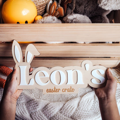 Wooden sign with 'Leon's Easter Crate' held by hands against a wooden crate background.