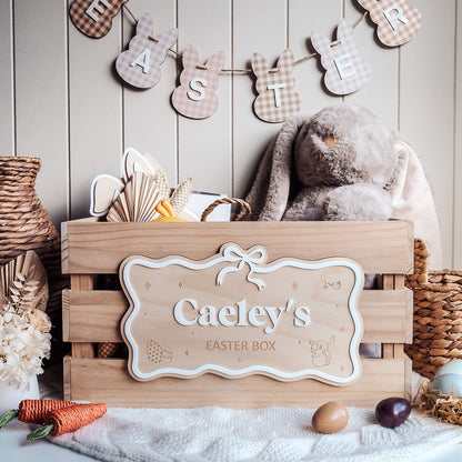 Wooden Easter box with 'Caeley's Easter Box' sign, teddy bear, and Easter decorations on a wooden background.