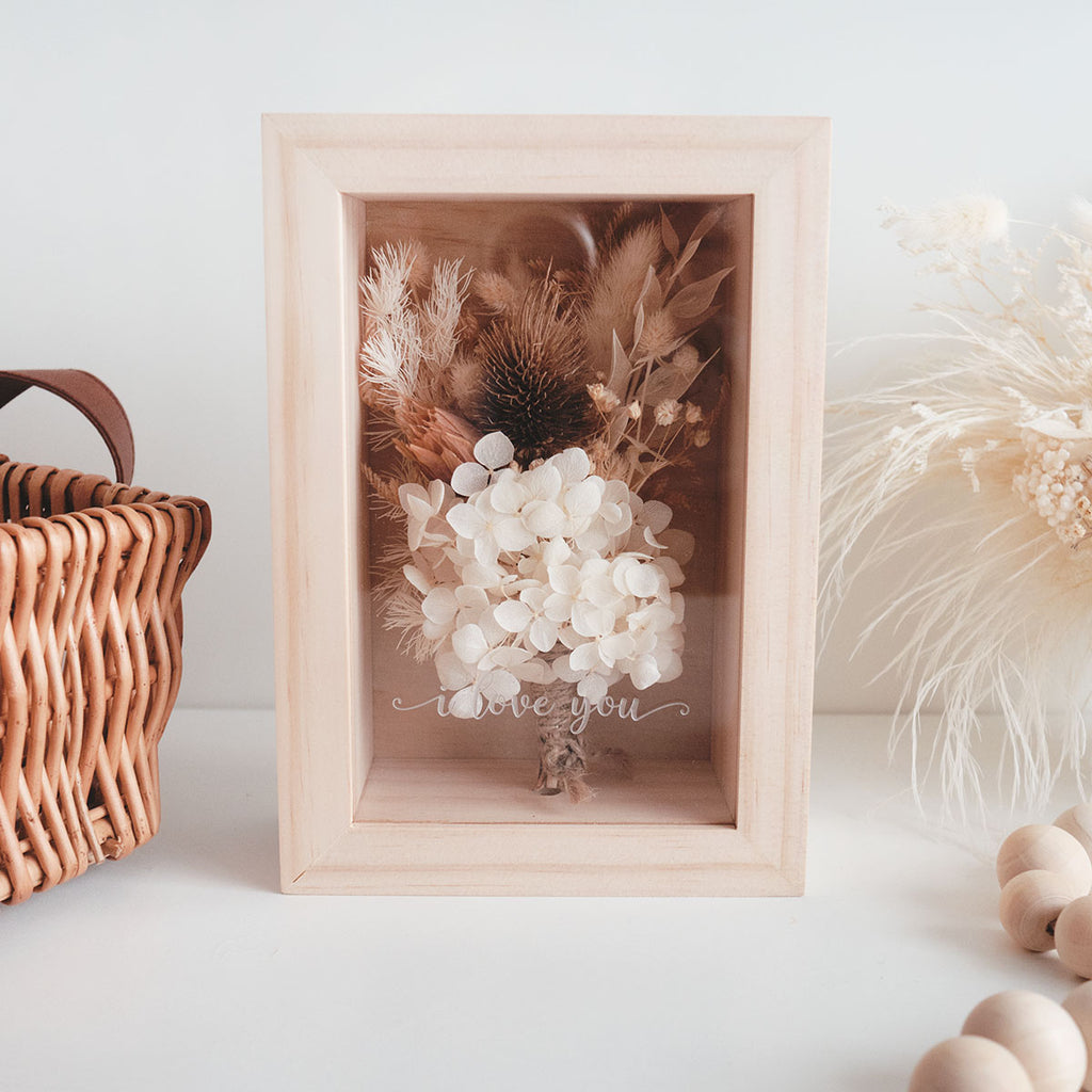 This is a wooden flower box with dried  natural brown and white flowers and  grass. This is a front view with thext "i love you"