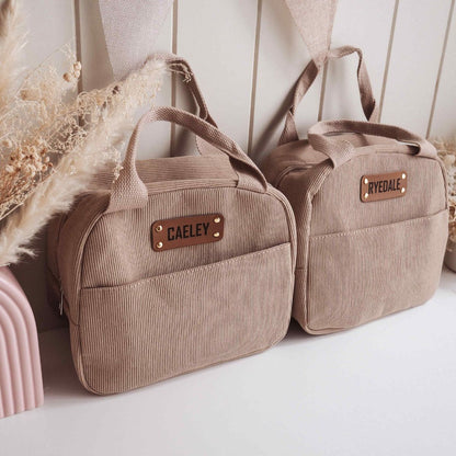 Two beige corduroy insulated lunch bags with personalized PU leather patches, one engraved with 'CAELEB' and the other with 'RYLDALE'.