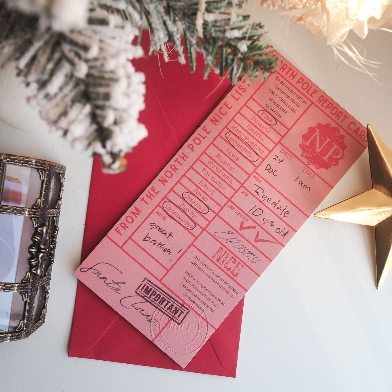 Pink North Pole Nice List report card on a red envelope with Christmas decorations.