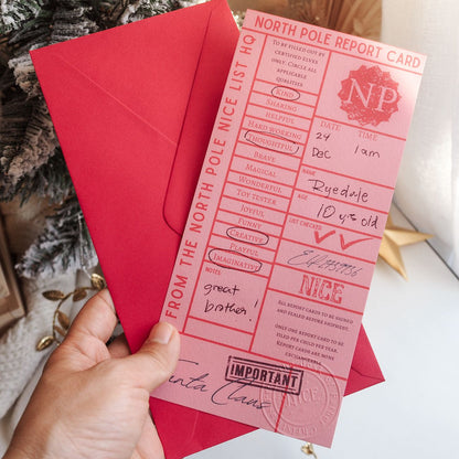 Hand holding a North Pole Report Card with a red envelope against a festive background.