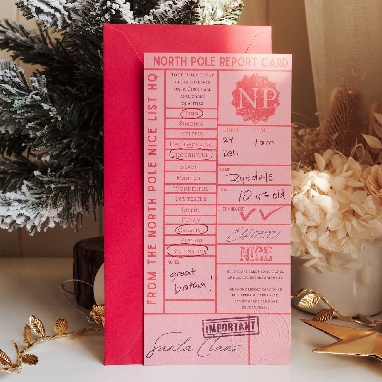 Pink 'North Pole Report Card' with Santa Claus signature on a decorative surface with Christmas elements.