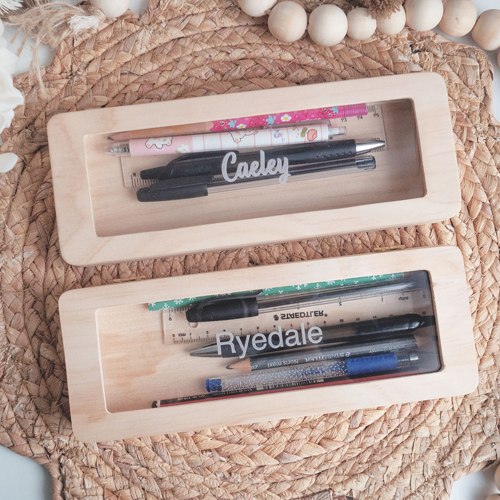 Personalised wooden pencil case made out of solid wood and clear acrylic. There's 2 pencil cases here with engraved names of Ryedale and Caeley