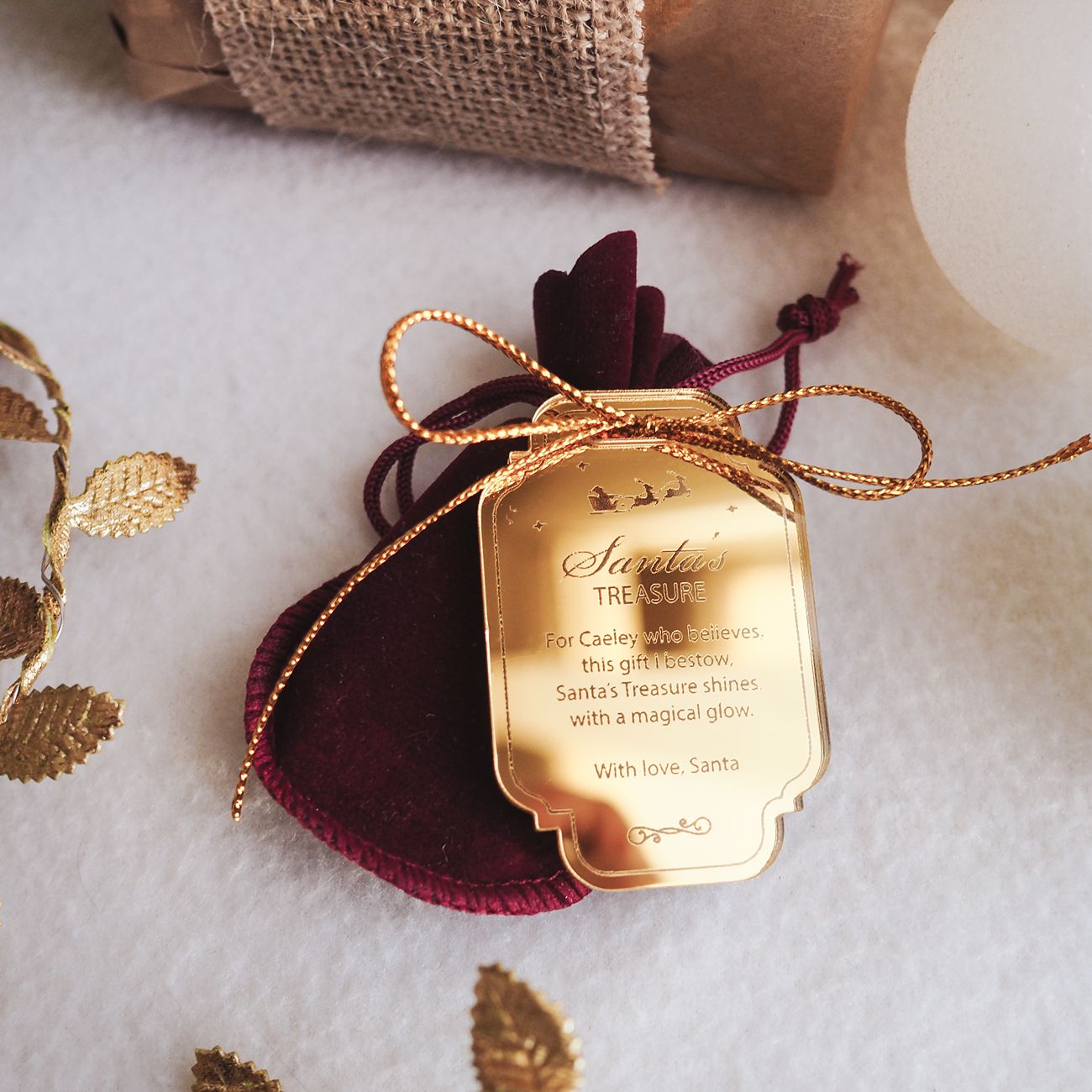 Gold 'Santa's Treasure' tag on a red fabric heart with gold ribbons, on a textured white surface.