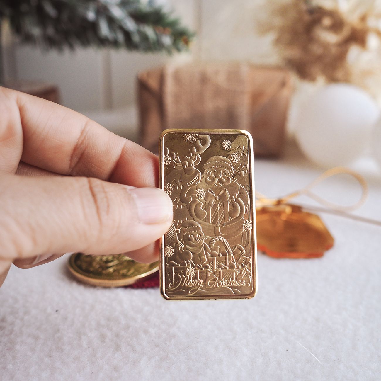 Hand holding a gold Christmas-themed bar with decorative elements on a light surface.