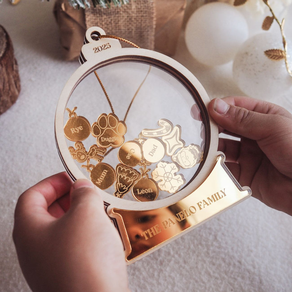 Decorative ornament with gold charms and 'The Paneo Family' engraving, held by a hand.