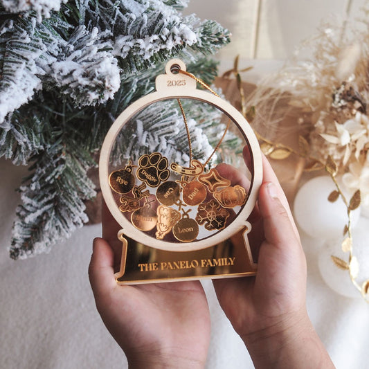 Decorative ornament with family names held in front of a Christmas tree.