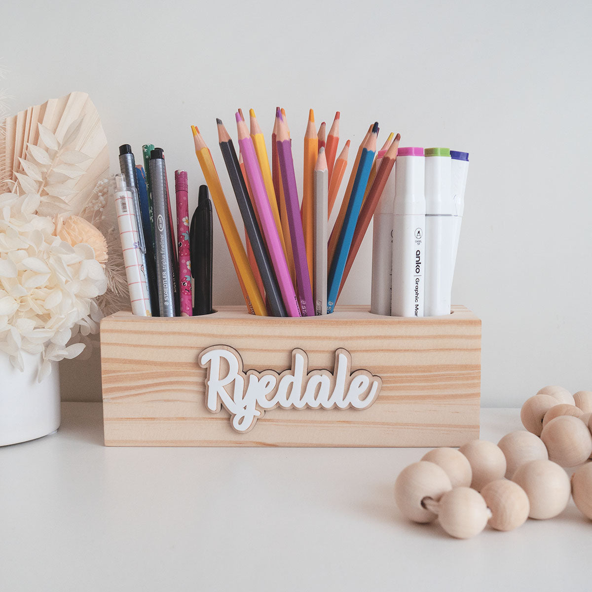 wooden pencil holder with three hole compartments. It is storing pencils, colour pencils and markers. It is also personalised.